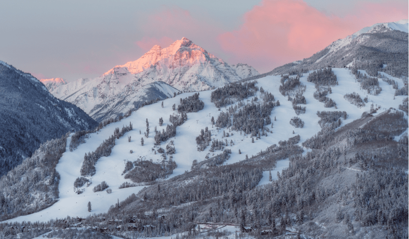 Buttermilk ski runsa at dawn, pink light highlights the maroon bells behind tiehack